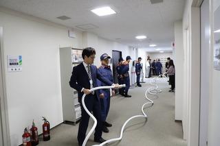 室内でホースを使って訓練をしている男性職員と、横で教えている消防職員の写真