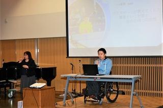 スクリーンの前で車椅子の男性が話をしている写真