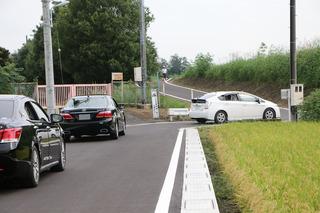 田んぼの横の開通した道路を3台の車が通っている写真