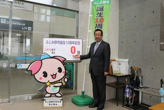 .市長が「ふじみ野市誕生10周年記念」と書かれてあるふじみんのパネルの横に立ち、パネルに表示されてある「0日」を右掌を上に向け示している写真