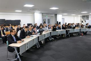 会場に机が並んでおり、市長が一番左横にに座っており、沢山の関係者の方々が発表を真剣に聞いている様子の写真