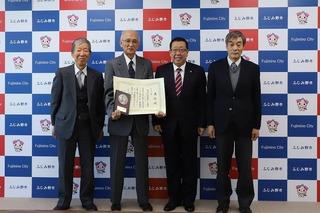 左から2番目の白髪の男性が賞状と盾を持ち隣に市長、両脇に関係者が並び4人で撮影した写真