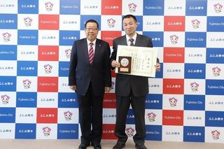 男性が賞状と盾を持ち、市長と2人で撮影した写真
