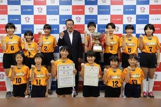 オレンジと黒のユニフォーム姿の女子小学生、大井クッキーズの皆さんと市長との記念写真
