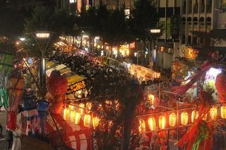 夜、提灯の明かりがともり屋台が賑わっている写真