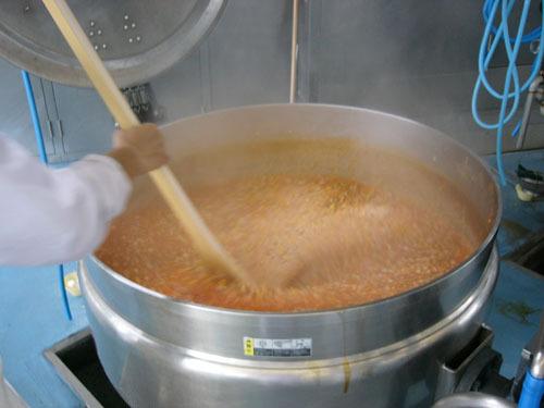 大きな釜と大きなヘラで給食を作っている写真
