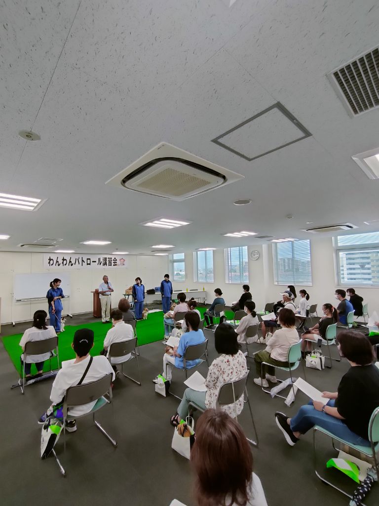 座っている講習会参加者の前にマイクを持った講師、実演者3人と犬3匹がおり、説明を行っている写真