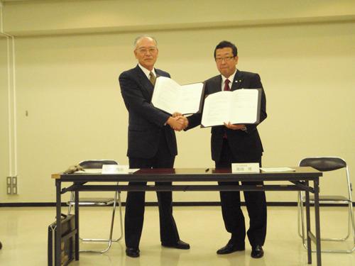協定書調印式で代表者と市長が調印書を持って握手をしている写真