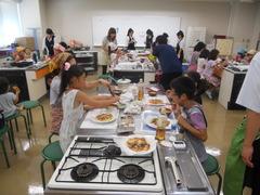 調理台の横で参加者の親子が作った料理を食べている写真