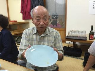 年配の男性が空になった大きなお皿を両手で持って見せている写真