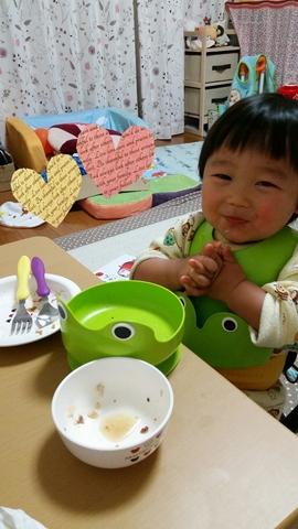 テーブルの上には空になったお皿が置かれていて、エプロンをつけた赤ちゃんがごちそう様をしようと手を合わせている写真