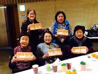 年配の女性5人が空になったお弁当箱を見せている写真