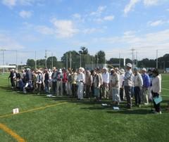 芝生の生えているグランドに、グラウンドゴルフ大会の参加者が大勢集まっている写真