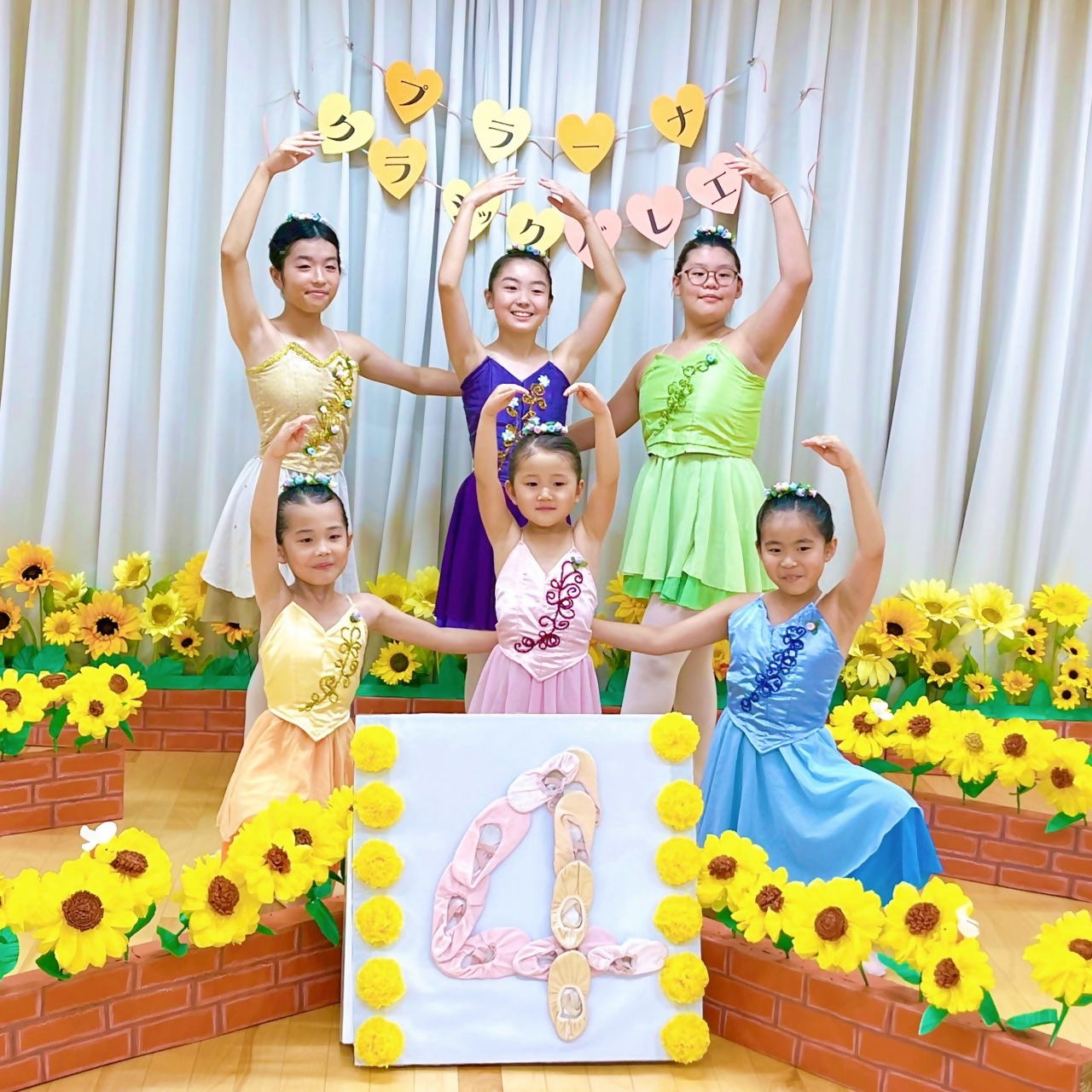 6人の女の子たちがバレエの衣装で数字の4のパネルを中心にポーズしている写真
