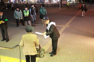 帽子を被り襷をかけた市長が街頭で市民に資料を配っている写真