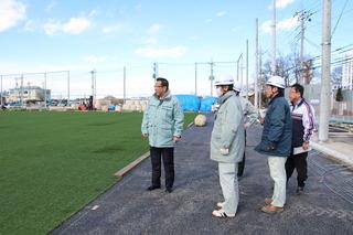 人工芝多目的グラウンドを工事現場のスタッフと見学している市長の写真