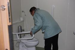 様式トイレの便器の横に設置されている手すりを握って市長が便器のを上から見ている様子の写真