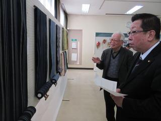 展示されているはたおり作品の説明を白髪の男性から聞いている市長の写真