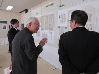 白髪の男性から案内を受けながら展示されている古文書を見学している市長の後ろ姿の写真