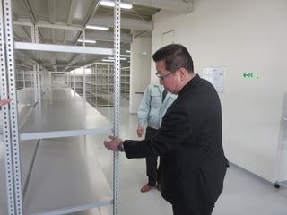 防災備蓄品管理倉庫に設置されたシルバーの棚を見ている市長の写真