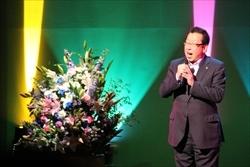 舞台上の、演台花の横で市長が歌を歌っている写真