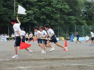 中学校の体育祭で生徒たちが竹の棒をチームで持ってコーンの周りを回っている写真