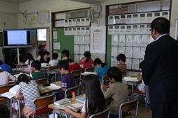 教室での授業で、子ども達が机に向かってノートに書き込んで学習している様子を、市長が教室の後ろから見ている写真