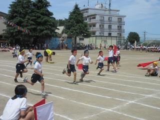 徒競走で青いハチマキと赤いハチマキを締めた児童がゴールに向かって一生懸命に走っている西小学校の運動会の写真