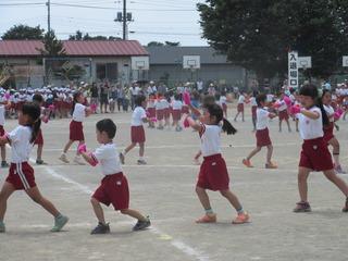 児童達がピンク色の手袋をはめて、大きな円を作って左方向を歩きながらダンスを踊っている大井小学校の運動会の写真