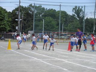 リレーの競技が行われており、青チームは前走者からバトンをもらって走りだしており、赤チームは前走者が走ってくるのを待ち構えている東台小学校の運動会の写真
