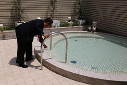 円形の浴室に水がなみなみと張られており、市長が手すりを持って、温度を確認している写真