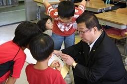 赤のシャツを着た子供達3人が教科書を市長に見せながら説明をしている写真