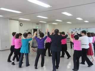 大勢の女性たちと輪になってつないだ両手を上にあげ「レクダンス」を踊っている市長の写真