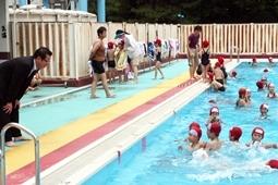 楽しそうにプールの中で泳いでいる赤の水泳帽姿の子供達にプールサイドから話しかけている市長の写真
