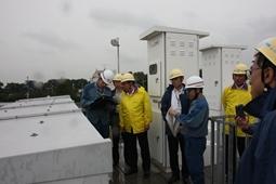 屋外で黄色の防寒着を着用した市長や見学者の人達に説明をしている変電所の人の写真
