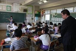 算数の授業で先生が黒板に図を描いているのを座って見ている生徒達を教室の後ろから見学している市長の写真