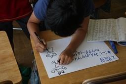 1人の紺のシャツをきた児童が画用紙に問題とイラストを描いている所を上から写した写真
