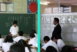 左：黒板の前に先生が立って授業が行われている写真、右：壁際で授業を見学する市長の写真