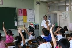 三角小学校にて授業中生徒が手を挙げている様子を入口付近で見学する市長の写真