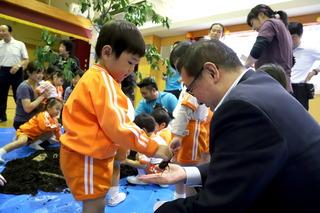 小さな男の子がカブトムシを右手で掴んで、市長の手のひらに乗せている写真