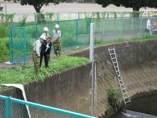 河川敷から、ホースが伸びている川の中を市長と関係者の男性がのぞいて話をしている写真