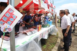 模擬店が沢山並んでおり、「大当たりあるよ」と書かれているお店の店主に市長が話かけている写真