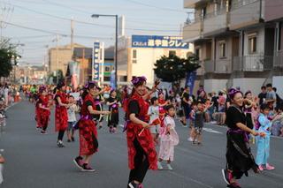 路上で、赤や黒の衣装を着けたダンスチームが元気よくダンスのパフォーマンスを見せている写真