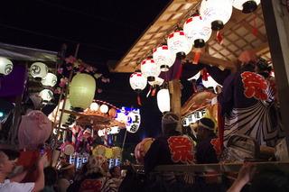 提灯の明かりが灯っている山車に、祭りの法被を着た人が乗っている写真