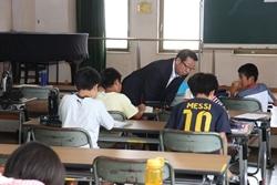 着席して学習する男の子の前で、中腰になって見ている市長の写真