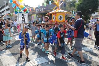 青い法被を着た子ども達が、「夢」と書かれているおみこしを元気よく担いでいる写真