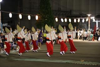 花笠を被って、赤と白の着物を着ている踊り子の方々が両手を上に挙げて、列を揃えて踊っている写真
