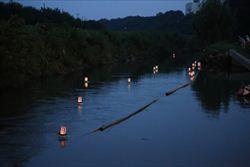 ろうそくの火が灯された灯籠が川にうかぶ写真