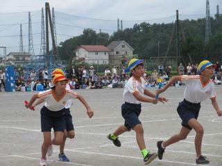 リレーの競技が行われており、中継地点で青いハチマキを締めた児童と、赤いハチマキを締めた児童が、バトンをもらって走り出そうしている写真