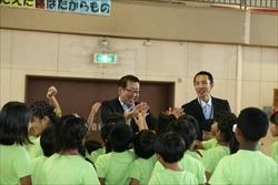 笑顔の市長の周りに集まり、ハイタッチをする三角小学校の3年1組の生徒たちの写真
